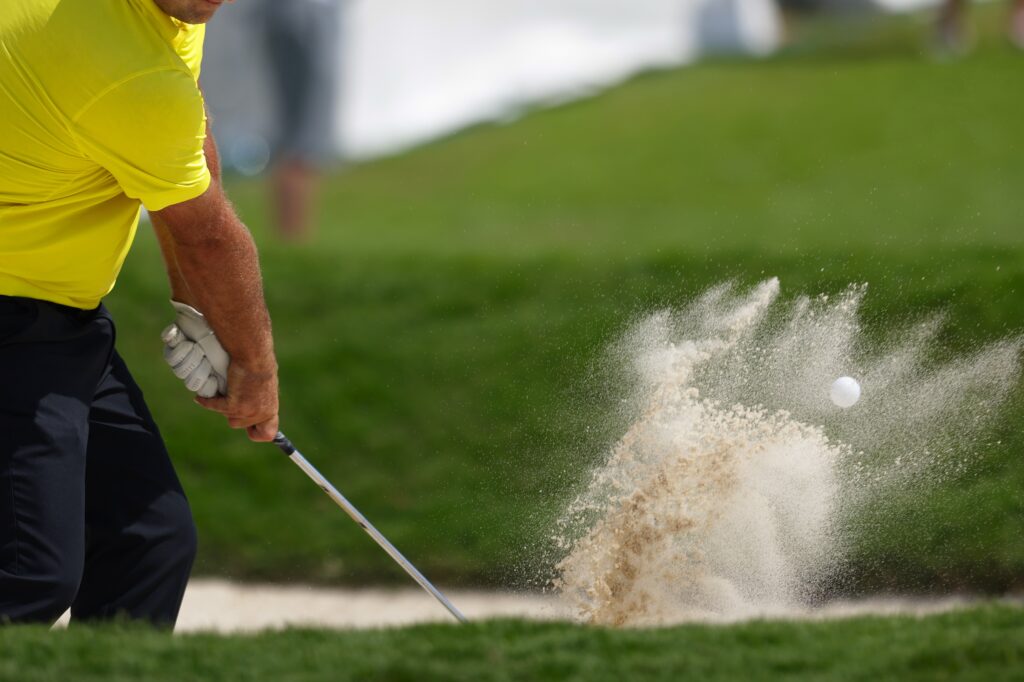 Golfer blasting out of a bunker during a tournament—PGA vs LIV Golf negotiation metaphor.